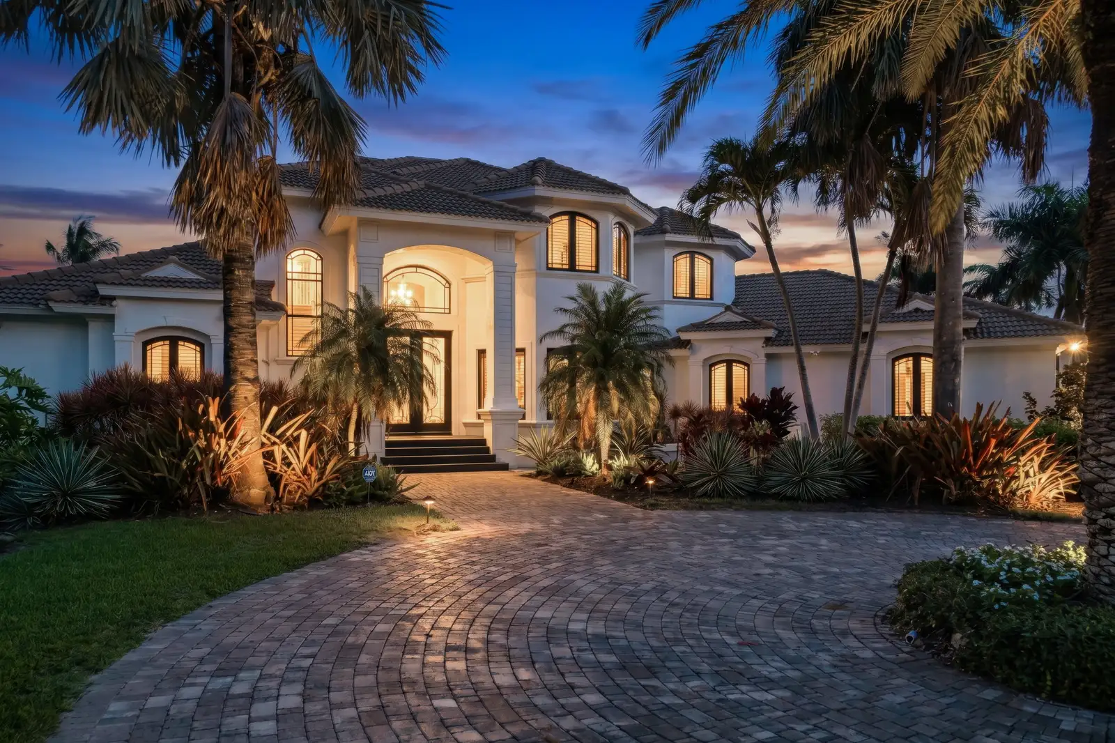 Your Property Address: Palm-lined entrance and illuminated home at twilight